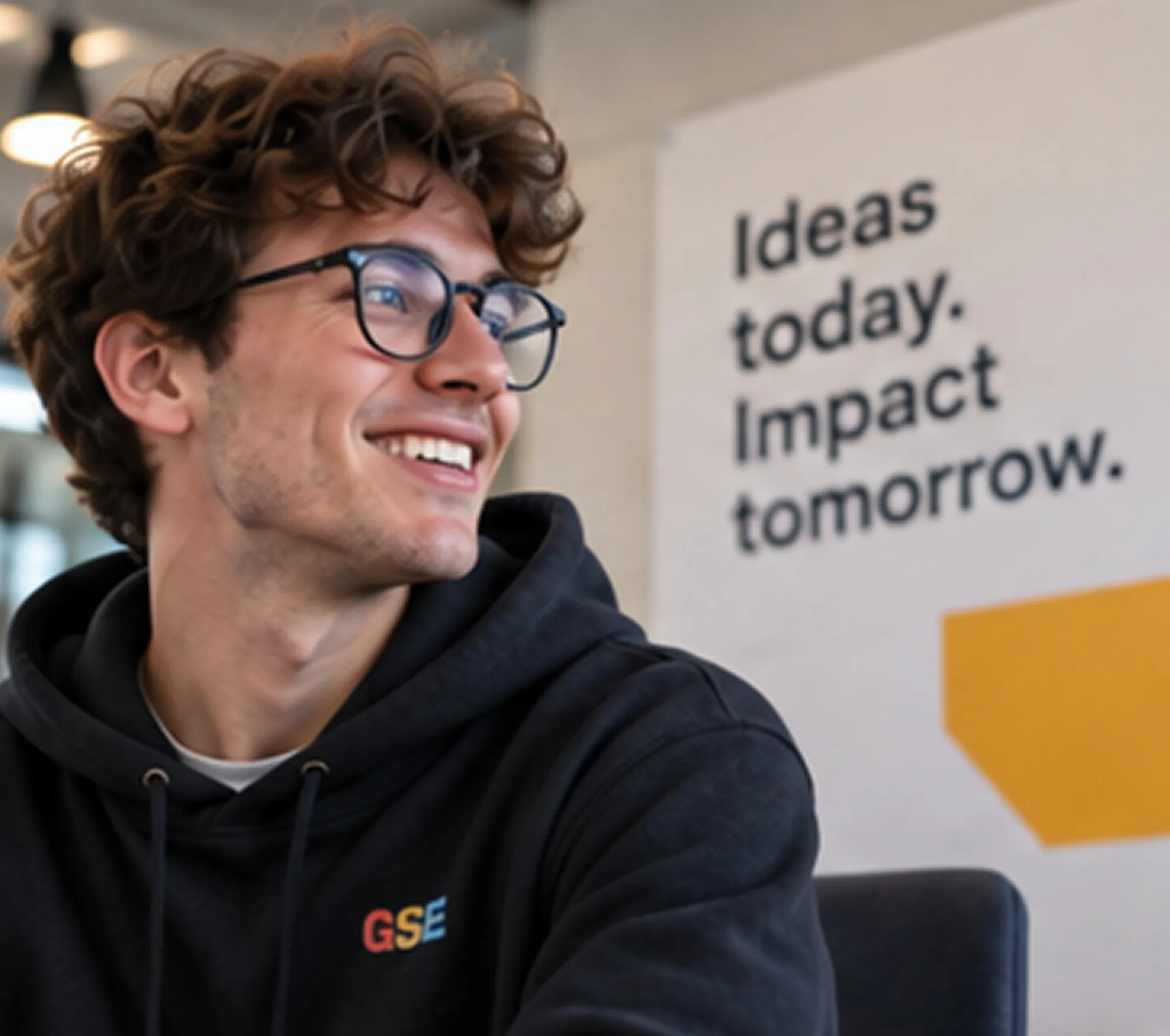 A smiling student in front of a poster reading “Ideas today. Impact tomorrow.”