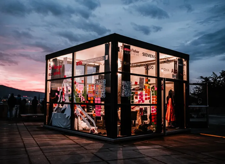 The InCube installation, a glass cube lit up at dusk.